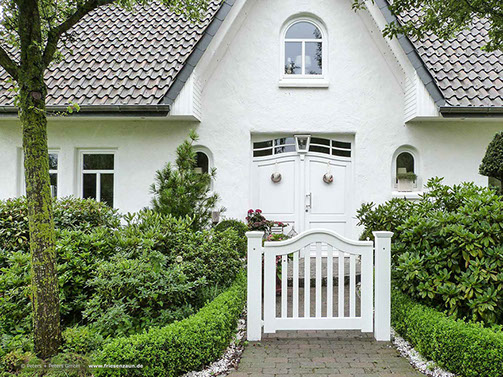 Schönes Landhaus im weißem Friesenstil mit grüner Bepflanzung - Buchsbaumhecke und weißer Holzpforte.